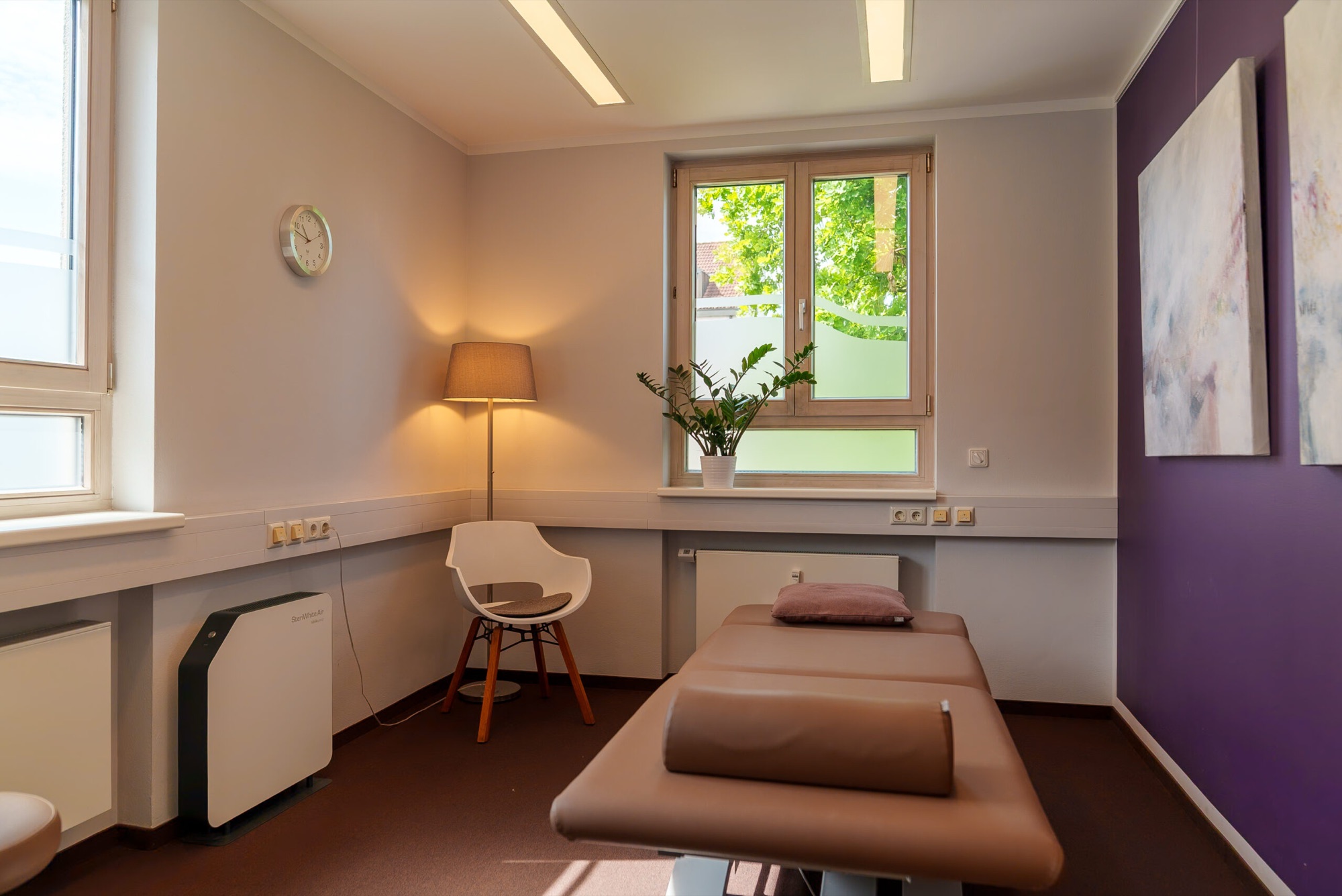 Heller Behandlungsraum der Praxis mit Therapieliege am Fenster